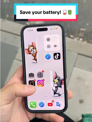 The cover image shows a hand holding an iPhone displaying its home screen. On the top, there is a text overlay in a rectangular box, with the text "Save your battery!". Below, the screen shows multiple app icons and a wallpaper split in two sections, with the cartoon characters Tom and Jerry peeking from each section of the screen.