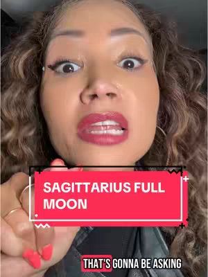 A selfie-style video cover featuring a woman with wide eyes and a surprised expression. Overlaid on her face are two text boxes: one red rectangle reading "SAGITTARIUS FULL MOON" in white text, and another red box displaying "THAT'S GONNA BE ASKING". The woman has dark curly hair, red lipstick, and appears to be wearing a black top.
