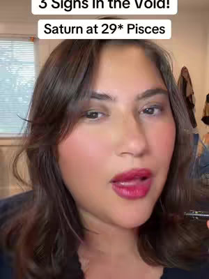 A close-up shot of a woman with brown hair and a dark top. The upper portion of the image features text overlays with white text inside black boxes. The woman has bright red lipstick and reddish blush. The background is a blurred indoors setting.