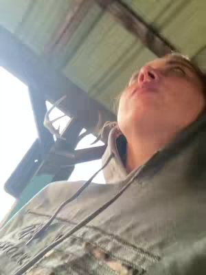 A low-angle shot features an individual looking upwards with the top of a building or structure visible above. The person is wearing a hooded sweatshirt, and a sunbeam shines from the left, creating highlights and shadows on the face and clothing. The composition is framed from the chest up.