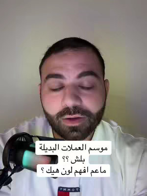 A man with a beard is centered in the frame, looking at the camera with a neutral expression. Text overlays are present towards the bottom half of the image. A microphone is positioned slightly to the left of the man. The background is a plain, light-colored wall.