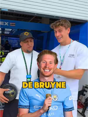 The cover image features three men. In the foreground, a man with red hair is smiling and holding a microphone. Behind him are two other men, one on each side, also smiling. The central man has a text overlay at the bottom that says "DE BRUYNE". The background appears to be a blue garage area.