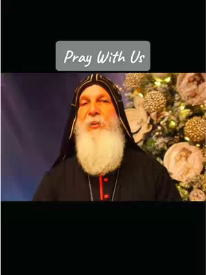 The image features a man with a white beard wearing a black robe with gold and red trim. He is positioned in front of a blurry Christmas tree. Above the man is a gray rectangle with the words "Pray With Us" in white text. The background is dark with purple and gold colors.