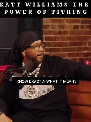 The image prominently features Katt Williams speaking into a microphone, with text overlays indicating the topic, 'The Power of Tithing'. He's wearing a black head covering, glasses, and a black sweatshirt with a logo. The background is a brick wall and the setting appears to be a podcast or interview setup.
