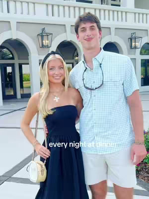 A couple posing in front of a building with archways. The woman wears a black strapless dress and a headband, with a small purse. The man wears a light blue checkered shirt and white shorts, with sunglasses hanging on his shirt. Text overlay "every night at dinner".