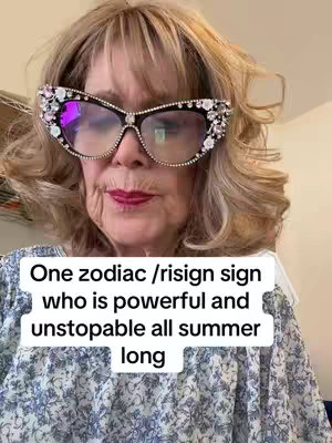 A woman wearing large, jeweled eyeglasses is looking directly at the camera. Her blonde hair is styled in loose waves. She is wearing a patterned blouse. A text overlay states, "One zodiac /risign sign who is powerful and unstoppable all summer long." The background appears to be an interior.
