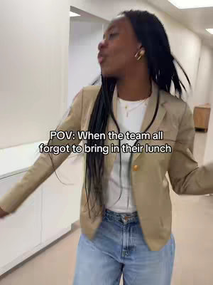 A woman wearing a blazer and jeans is walking and talking in a hallway