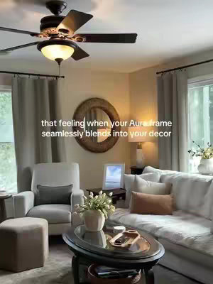 The cover image showcases a well-lit, cozy living room. The focus is on the decor, featuring a white sofa with several decorative pillows, a coffee table with a decorative display, and a mirror above the sofa. Text overlayed on the image reads: "that feeling when your Aura frame seamlessly blends into your decor". The lighting is soft and natural, creating a warm and inviting atmosphere. The overall composition suggests a sense of comfort and style, emphasizing the digital photo frame's integration into the home's interior.