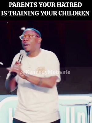 A man in a white shirt and glasses speaks into a microphone, with the text overlayed on top. He is located on a stage.