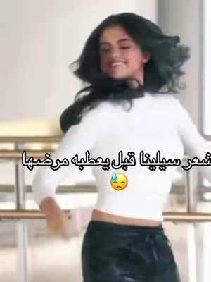 The image shows Selena Gomez dancing. She wears a white long-sleeve top and black pants. Text in Arabic is overlaid on the image, and the background is blurred.