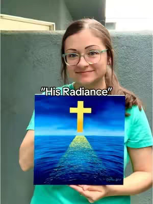 A woman with glasses holds a painting depicting a golden cross over water under a blue sky. Text overlayed explains that prints are available.
