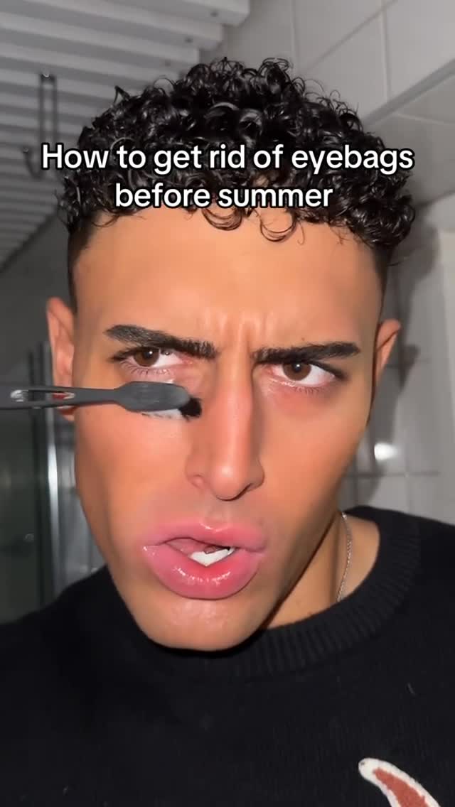 A close-up shot of a man with dark curly hair, holding a small, black brush near his left eye. He is looking intensely at the camera. The text overlay informs the content.