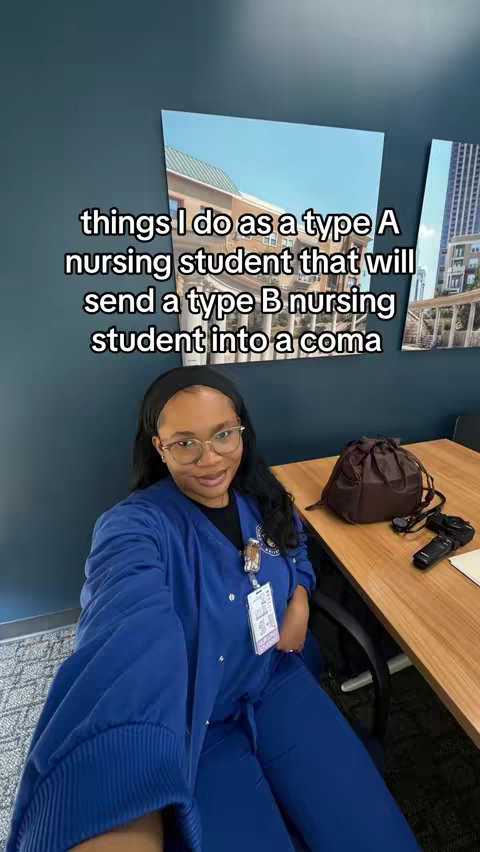 A selfie-style shot of a person in scrubs smiling and sitting at a desk. Overlay text is present. The background shows an office-like setting.