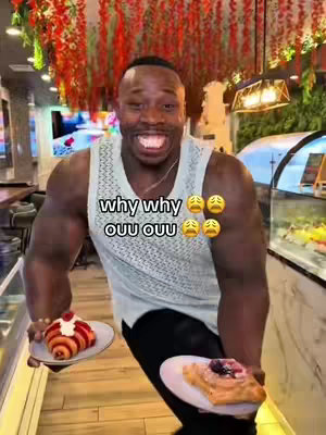 A man with a muscular build stands in what appears to be a cafe or restaurant setting. He is holding plates with pastries while smiling, with text overlaid on his shirt.