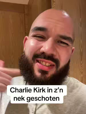 A man with a shaved head and a full beard is shown from the chest up in a close-up shot. He has a slightly concerned expression, and a text overlay at the bottom reads 'Charlie Kirk in z'n nek geschoten'. The background appears to be a wooden wall.