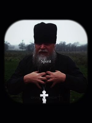 An image framed in a dark vignette. It features a man in a dark robe and hat, possibly a cleric or religious figure, at the center. He has a long, gray beard and is wearing a silver cross necklace. His hands are clasped over his chest. The background is a blurred outdoor scene with a somewhat overcast sky. The word "Spirit" is superimposed on the image.