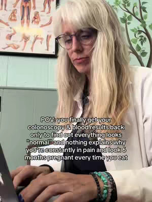 The image shows a woman with long blonde hair and glasses, wearing a white coat, looking down at a laptop on a wooden desk. Behind her are medical diagrams on the wall and a green painted wall. Text is overlaid on the image.