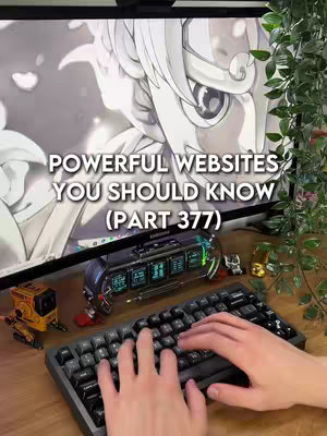 The image features a desk setup with a computer screen displaying an anime-style drawing in the background. In the foreground, there is a black keyboard and a small industrial-looking device with several screens. A hand is typing on the keyboard. The scene is framed with leafy green plants on the sides.