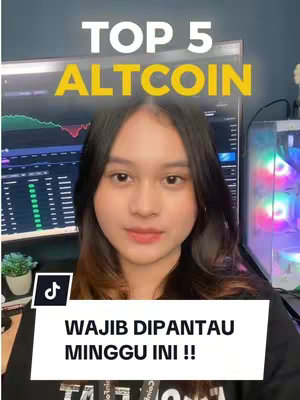 A young woman with long dark hair is centered in the frame of a vertical video. She is smiling slightly. Behind her, a computer monitor displays a stock chart, suggesting financial content. The background includes additional computer equipment and a plant, giving context to the setting.