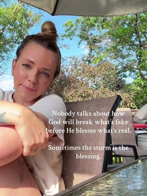 A woman with a bun in her hair sits outside, looking towards the camera. She's wearing a white top, and partially obscuring the view with her arm. Text overlays are present.