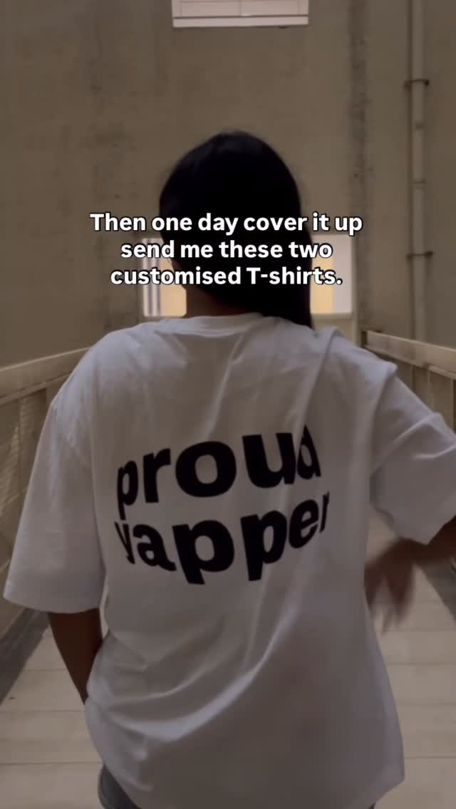 The image shows a person from the back, wearing a white t-shirt. The t-shirt has the words 'proud rapper' printed on it. The person is walking down a hallway, with a neutral background.