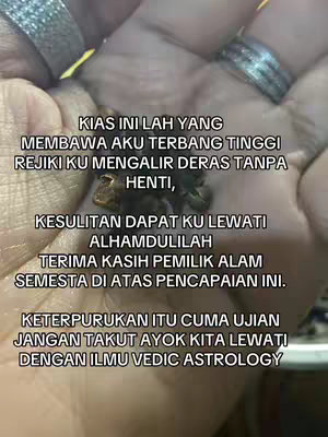 A close-up shot of a hand holding a dark, possibly organic object, with text overlays in a script font. The background is blurred, suggesting a soft focus. The hand appears to be wearing two rings.