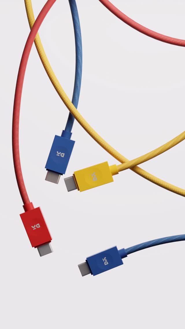 An overhead shot displays four charging cables against a plain white background. The cables are suspended in the air and are arranged in an overlapping and slightly chaotic manner. Each cable is a different vibrant color - one red, one yellow, one blue, and the fourth red, with a white background. The connectors have the brand logo.