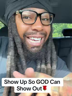 A smiling Black man wearing glasses and a black head covering poses for the camera. The background is a car interior and a glimpse of trees through the window. Text overlayed on the image says: Show Up So GOD Can Show Out with a rose emoji.