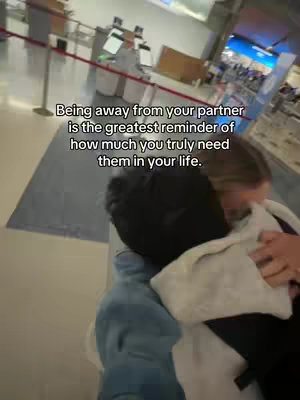 A candid shot inside an airport. Two people are embracing, their faces partially obscured, suggesting a reunion or farewell. Text overlayed on the image conveys a message about long-distance relationships and the value of partnership.