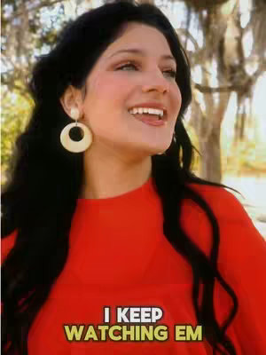 A woman with long black hair smiles, looking towards the right. She has large, circular cream-colored earrings and is wearing a red top. Text overlays the lower portion of the image.