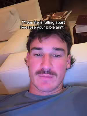 A man with dark hair and a mustache looks directly at the camera against a background of a couch and an open book. Text overlayed on the image reads "Your life is falling apart because your Bible ain't."