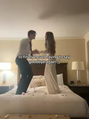 A couple is shown jumping and holding hands on a bed with a backdrop of a room with warm lighting. Text is overlaid across the bottom of the image.