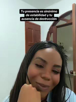 A woman with long black hair and a slightly smiling expression. She is in front of a white wall and some of a door. The text overlay says: 'Tu presencia es sinónimo de estabilidad y tu ausencia de destrucción'.