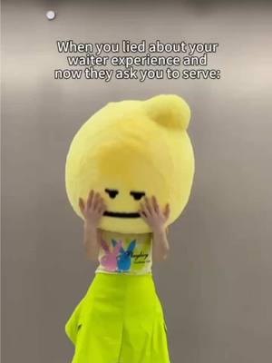 A person is wearing a lemon costume, with a large yellow head covering their face and arms raised, touching the head. Their torso and legs are visible, wearing a white t-shirt with a print of bunnies and a green skirt.