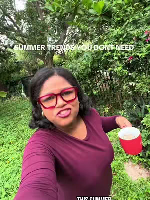 A woman with dark hair and glasses holds a red mug, standing in front of green foliage. The background is filled with lush greenery.