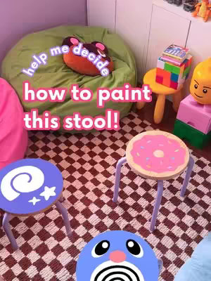 The cover image showcases a brightly lit room with various colorful furniture pieces and objects, featuring the text overlay "help me decide how to paint this stool!". In the foreground, three small stools with unique designs are presented. The background includes a green beanbag, a pink pillow, and a checkerboard floor pattern, lending to a playful and maximalist aesthetic.