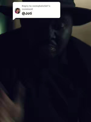 A close-up shot of a Black man from the chest up, wearing a black hat with a dark background. The man's face is lit, and he has a serious expression. A comment box is positioned in the upper left corner of the frame.