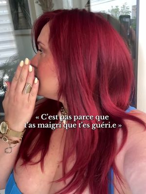 The cover photo features a woman with vibrant red hair, facing left with her hand covering her mouth. She is wearing a watch and a ring. The background is softly blurred with a window visible. Text overlaid on the image reads, "C'est pas parce que t'as maigri que t'es guéri.e".