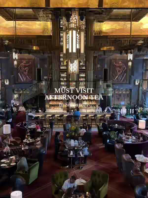A high-angle shot of a luxurious bar and lounge. The space has a grand, art-deco style with ornate architecture, including a central bar area, seating arrangements, and a staircase. The color palette includes gold, dark wooden tones, and deep reds. The composition is balanced, with layers of elements creating depth, and it's well-lit, highlighting the elegance of the setting.