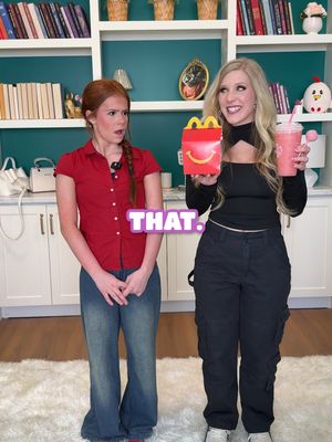 Two women stand facing each other in a bright room. One holds a Happy Meal box and a pink drink, while the other observes with a surprised expression. A text overlay reading "THAT." is on the image.