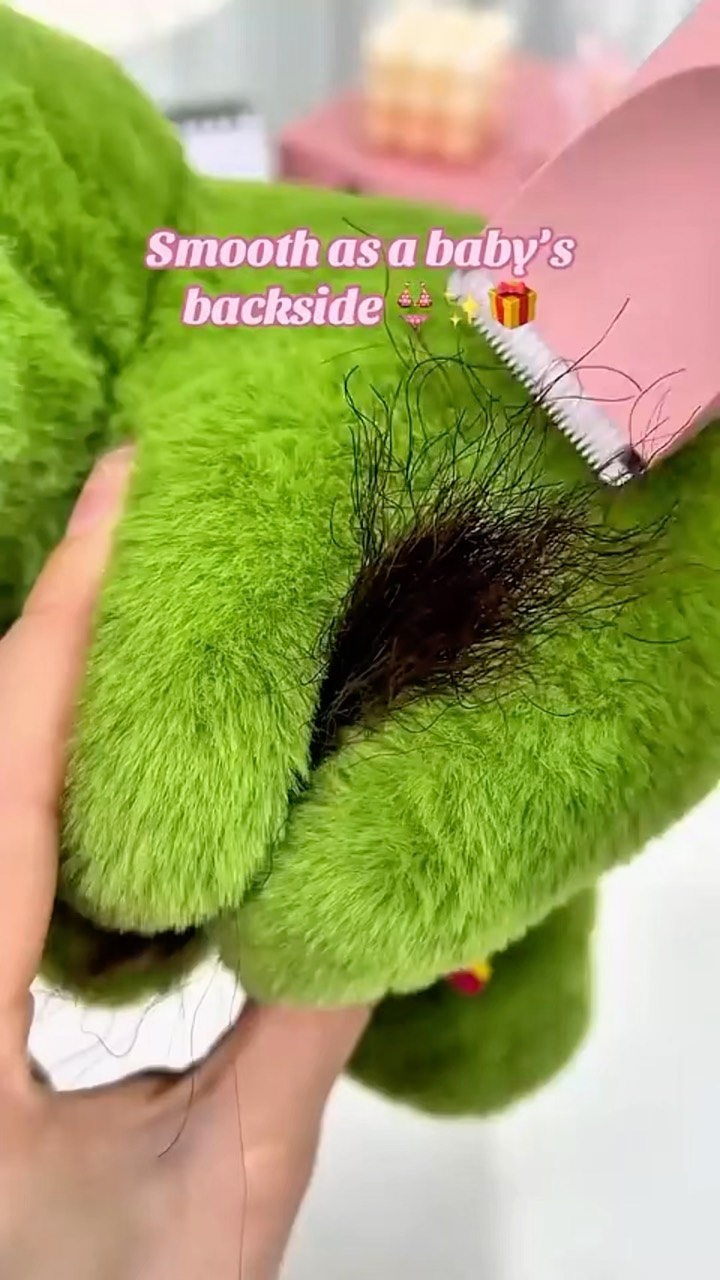 The cover image displays a close-up of a plush green material with a dark patch suggestive of pubic hair. A pink electric trimmer is positioned to shave the hair. Text overlays read: 'Smooth as a baby’s backside'. The overall composition seems designed to be attention-grabbing and possibly humorous.