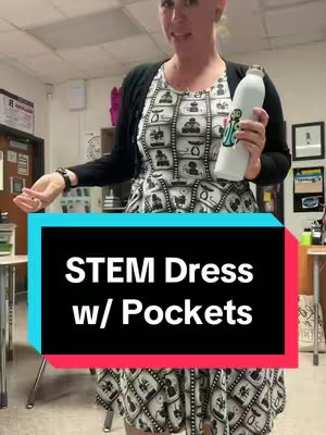 A woman in a patterned dress and a black cardigan poses in what appears to be a classroom. Text overlayed on a bright blue rectangle reads 'STEM Dress w/ Pockets'. She is holding a water bottle and there are desks and items in the background. 