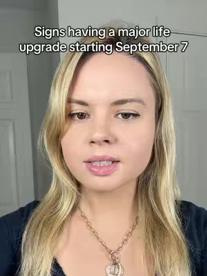 A woman with blonde hair is centered against a plain wall background. The cover image highlights her face, and she wears a necklace with a heart pendant. Text overlay is visible at the top, while the bottom half of the frame shows her dark blue top.