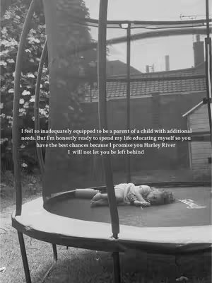 A black and white photo shows a young child lying on a circular trampoline bed. The trampoline is situated outdoors, with the netting of the trampoline and poles in the foreground. The background includes out-of-focus greenery and what appears to be a house. Text is superimposed on the image, and the overall tone is somber.