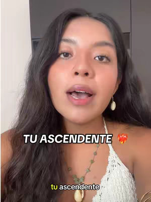 A medium shot of a woman with long dark hair looking directly at the camera and talking. She's wearing a white top and a necklace. The text overlay says "TU ASCENDENTE." The colors are natural with soft skin tones and a background that appears to be indoors.