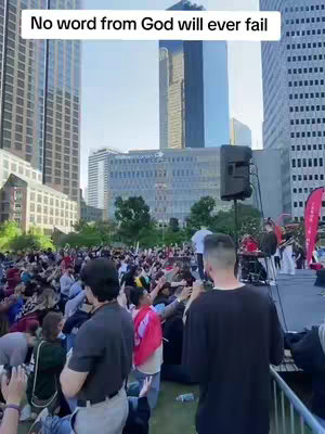 An outdoor scene with a large crowd of people, tall buildings in the background, and a stage with sound equipment. Text overlayed at the top of the image reads: 'No word from God will ever fail'.
