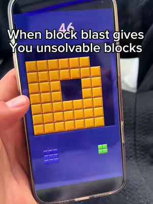 A person's hand holding a phone displaying the Block Blast game. The game screen shows a level with a mostly filled grid of orange blocks. White text over the screen reads "When block blast gives You unsolvable blocks". Below the game, there are two small blocks, a blue one with four squares and a green one made of four squares. The background is black.