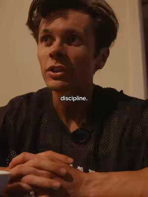 A medium shot of a young man in a black mesh shirt, talking. The background is a neutral color. The text 'discipline' is overlaid on the image.