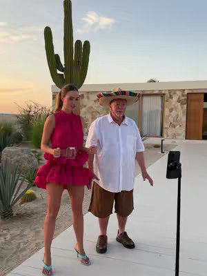A woman and a man in a sombrero on a sunny day. The woman is in a short pink dress, holding the man's arm