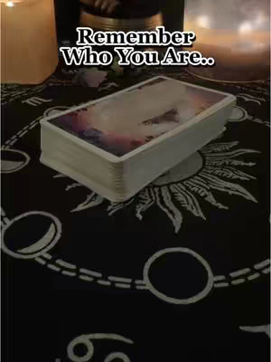 The cover image showcases a deck of tarot cards resting on a black cloth adorned with celestial patterns. The words 'Remember Who You Are' sit prominently above the cards, hinting at the video's theme. Two candle flames are partially visible near the top left corner, adding soft lighting to the spiritual atmosphere. The overall composition is centered, emphasizing the tarot deck as the main focus.